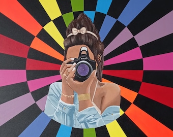 May include: A woman with a bow in her hair holds a black camera in front of her face. The background is a colorful radial pattern of black, red, orange, yellow, green, blue, purple, and pink.