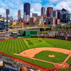 Puede incluir: Vista aérea del PNC Park, un estadio de béisbol, con un campo verde y el horizonte de Pittsburgh al fondo. El campo tiene un gran logotipo "P". El estadio está lleno de espectadores.