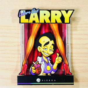 Puede incluir: Una caja de juego de ordenador vintage "Leisure Suit Larry". La caja presenta un personaje de dibujos animados haciendo una señal de pulgar hacia arriba, con el título del juego en amarillo y negro. El personaje está frente a una cortina roja y piernas con tacones altos.