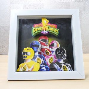 May include: A framed print of the Mighty Morphin Power Rangers. The image displays the team in their iconic coloured suits: yellow, blue, red, pink, and black. The white frame provides a clean, contemporary aesthetic to the artwork.
