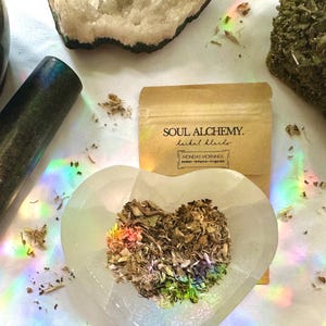 Pode incluir: Um saco de papel castanho com o texto "SOUL ALCHEMY. herbal blends" e "MONDAY MORNINGS awaken - enhance - invigorate". O saco contém uma mistura de ervas secas num tazón branco em forma de coração.