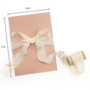 Peut inclure: Une carte rose blush, de 12,7 cm de large et 17,8 cm de haut, est attach&eacute;e avec un ruban cr&egrave;me. Une bobine du m&ecirc;me ruban, de 2,5 cm de large, est &agrave; proximit&eacute;. Le ruban a un bord effiloch&eacute;.