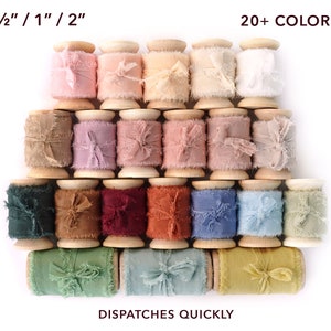 Peut inclure: Collection de rubans color&eacute;s &agrave; bords effiloch&eacute;s sur des bobines en bois. Les rubans sont disponibles dans une vari&eacute;t&eacute; de couleurs pastel et de bijoux, avec le texte "1/2" / 1" / 2"" et "20+ COLORS" visibles. Le texte "DISPATCHES QUICKLY" est &eacute;galement visible.