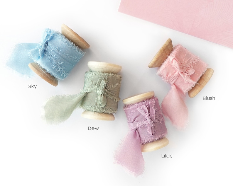 Peut inclure: Quatre bobines de ruban d&eacute;coratif dans les couleurs bleu ciel, vert ros&eacute;e, rose blush et lilas. Chaque ruban est enroul&eacute; autour d'une bobine en bois et pr&eacute;sente un bord effiloch&eacute;. Les noms des couleurs sont imprim&eacute;s en dessous.