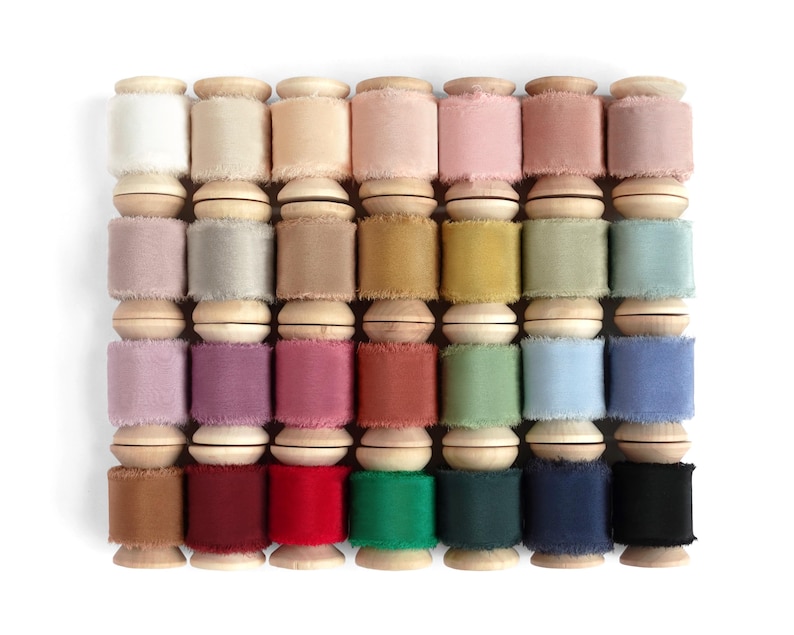 Peut inclure: Une collection de rubans de soie color&eacute;s sur des bobines en bois. Les rubans pr&eacute;sentent diverses nuances, notamment du blanc, du rose, du vert, du bleu et du marron. Les bobines sont dispos&eacute;es en grille, mettant en valeur la vari&eacute;t&eacute; des couleurs et des textures.