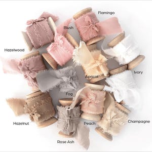 Peut inclure: Collection de bobines de rubans d&eacute;coratifs de diff&eacute;rentes couleurs, dont rose, beige et gris. Chaque bobine est &eacute;tiquet&eacute;e avec un nom de couleur, comme "Hazelwood", "Blush" et "Fog". Les rubans ont un bord effiloch&eacute;, ajoutant une touche rustique.