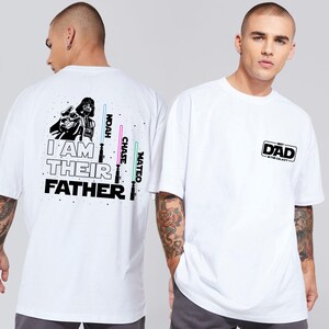 May include: White t-shirt with a black and white image of Darth Vader on the back. The text "I am their father" is printed below the image. The text "Noah, Chase, Mateo" is printed to the right of the image. The front of the shirt has the text "Best Dad in the Galaxy" printed on it.