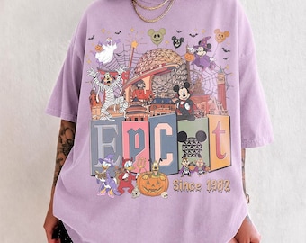 May include: A light purple t-shirt featuring a graphic print of Disney characters in Halloween costumes, the Epcot geodesic sphere, and the text "EPCOT Since 1982". The design includes Goofy as a mummy, Mickey Mouse as a vampire, and Donald Duck.