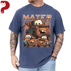 May include: Blue t-shirt featuring the word "MATER" above a graphic of the character Mater from the animated movie Cars. The graphic shows Mater and two other similar tow trucks with smiling faces. The shirt is a solid blue color.