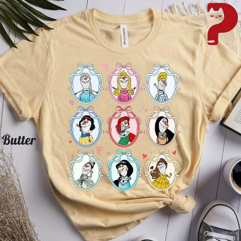 May include: Butter-colored t-shirt featuring a design of cartoon characters in oval frames with bows and hearts. The characters are in various outfits and poses. The shirt is made of a soft material.