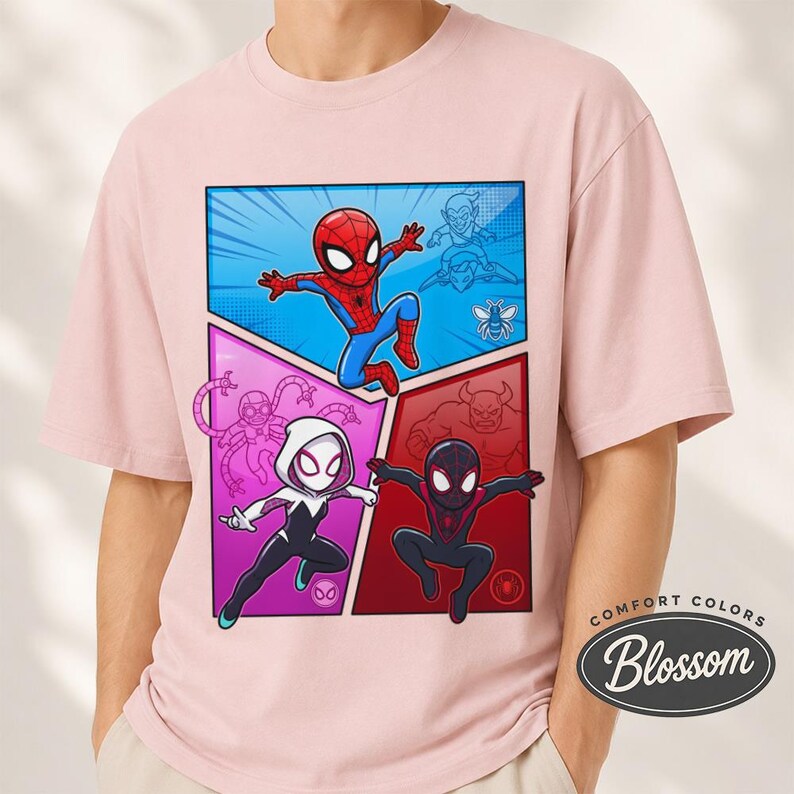 May include: A light pink t-shirt featuring a comic book style graphic of Spider-Man and two other Spider-Verse characters. The graphic is divided into three sections with blue, purple, and red backgrounds. The shirt has the text "Comfort Colors Blossom".
