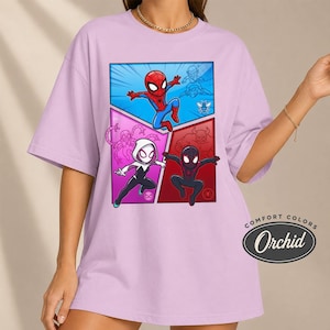 May include: A light purple t-shirt featuring a comic book style graphic of Spider-Man and two other Spider-Verse characters. The graphic is divided into three sections with a blue, pink, and red background. The shirt has the words "COMFORT COLORS" and "Orchid" printed on the bottom right.