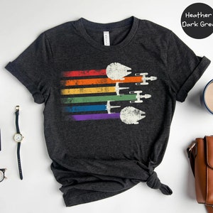 May include: A heather dark grey t-shirt featuring a rainbow stripe design and a vintage-style image of multiple Star Wars Millennium Falcon spaceships flying in formation.