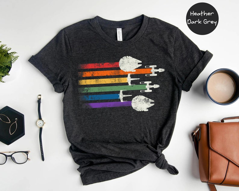 May include: A heather dark grey t-shirt featuring a rainbow stripe design and a vintage-style image of multiple Star Wars Millennium Falcon spaceships flying in formation.