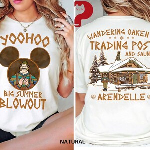 May include: Cream-colored t-shirt with a front graphic featuring a cartoon character within Mickey Mouse ears and text that reads "Yoohoo Big Summer Blowout." The back of the shirt displays "Wandering Oaken's Trading Post and Sauna" with a cabin illustration.