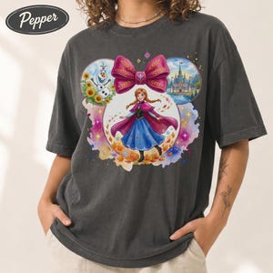 Puede incluir: Camiseta gris oscuro con un gr&aacute;fico colorido de Anna de Frozen, un gran lazo rosa e im&aacute;genes de Olaf y un castillo. La camiseta tiene un corte holgado y mangas cortas. La palabra "Pepper" est&aacute; impresa en la parte superior izquierda.