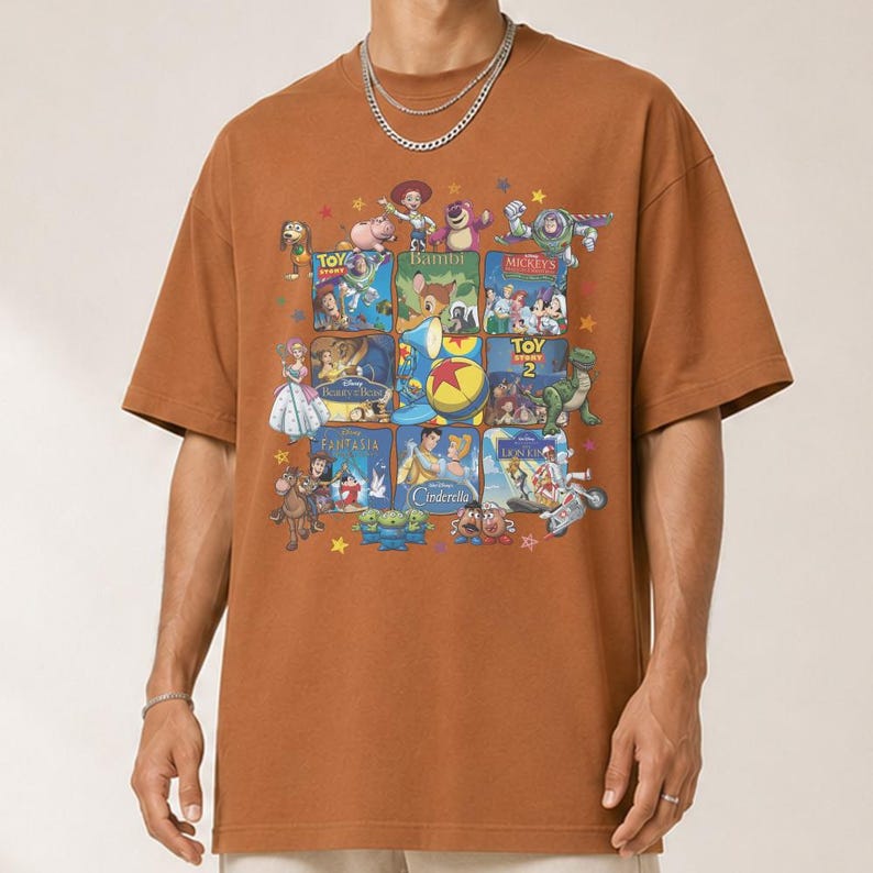 May include: A brown t-shirt featuring a collage of Disney movie posters, including Toy Story, Bambi, and Cinderella. The design is surrounded by stars. The shirt has short sleeves and a crew neck.