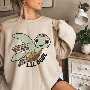 May include: A beige sweatshirt with a cartoon sea turtle graphic and the text "Lil Dude".