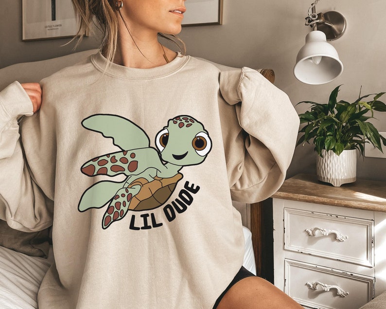 May include: A beige sweatshirt with a cartoon sea turtle graphic and the text "Lil Dude".