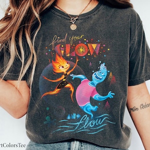 May include: A black t-shirt with a distressed look featuring a graphic of two cartoon characters. The text "find your glow and flow" is printed on the shirt.