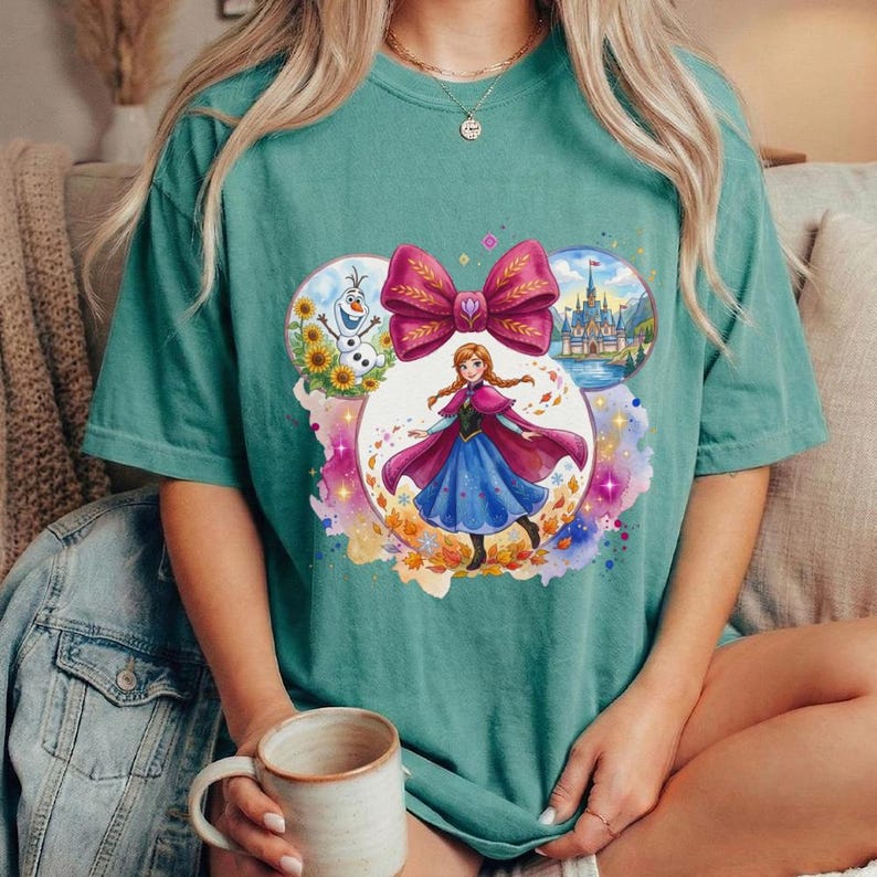Puede incluir: Camiseta de color verde azulado con un gr&aacute;fico de princesa de Disney. El dise&ntilde;o incluye un gran lazo, la princesa e im&aacute;genes de un castillo y Olaf el mu&ntilde;eco de nieve. La camiseta es de estilo c&oacute;modo e informal.