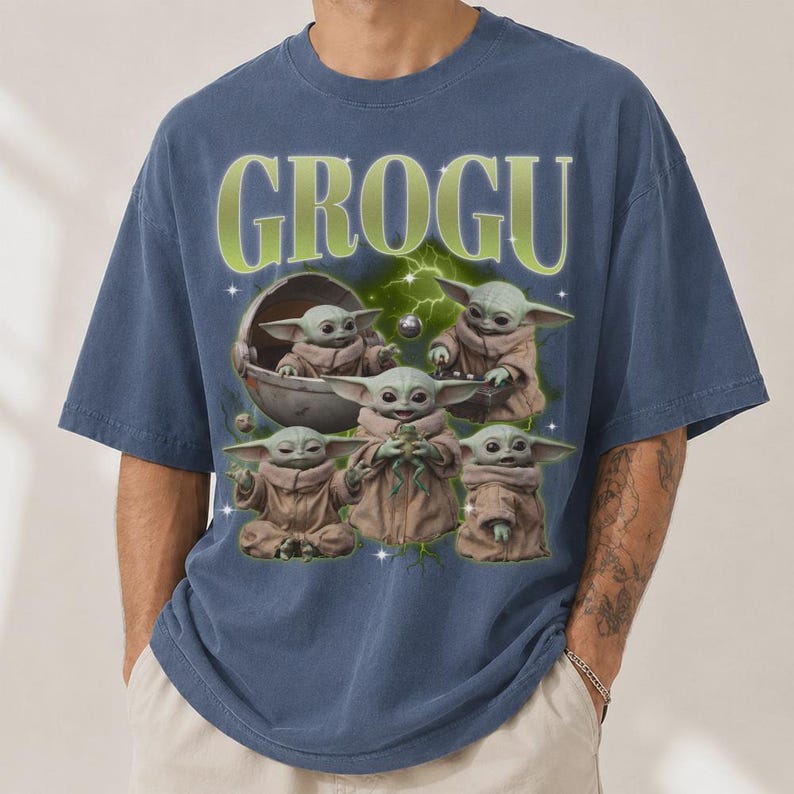 May include: Blue t-shirt featuring the word "GROGU" in green lettering. The shirt displays a graphic of Grogu, also known as Baby Yoda, in various poses. The design includes a space theme with lightning and a pod.