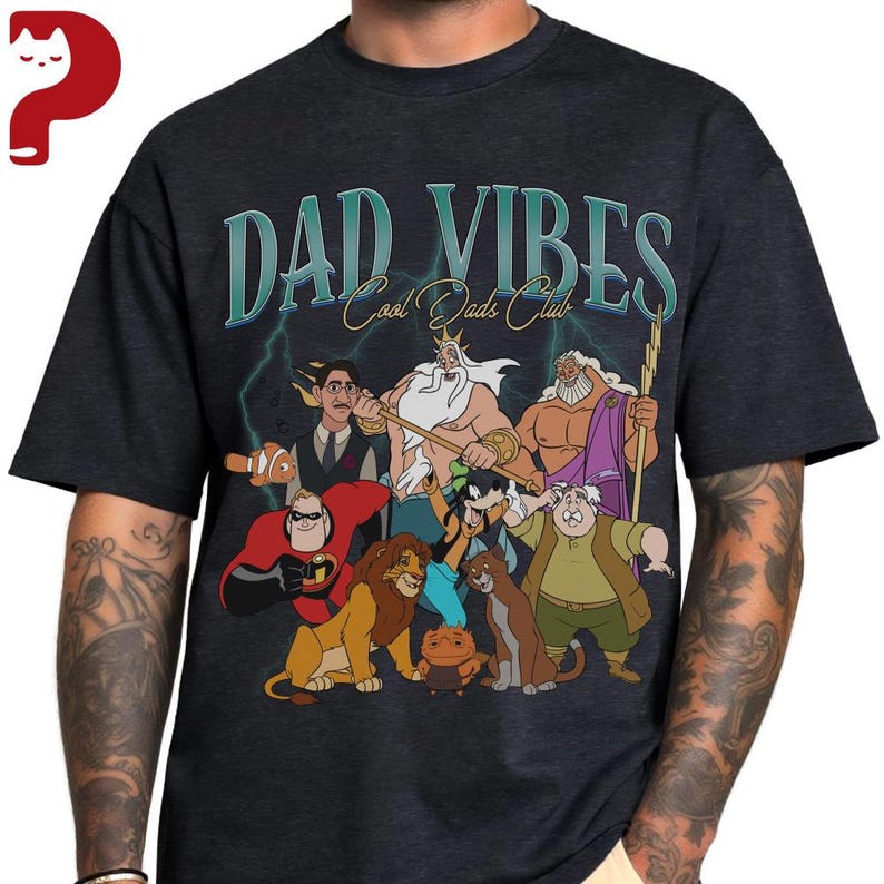 Peut inclure: T-shirt gris fonc&eacute; avec l'inscription "DAD VIBES Cool Dads Club" en lettres turquoise. Le t-shirt pr&eacute;sente des illustrations de personnages de dessins anim&eacute;s, dont un poisson, un lion et un super-h&eacute;ros.