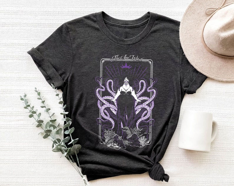 May include: A dark gray t-shirt with a graphic print of Ursula, the sea witch from Disney's The Little Mermaid. The graphic features Ursula with tentacles and the text "The Sea Witch".