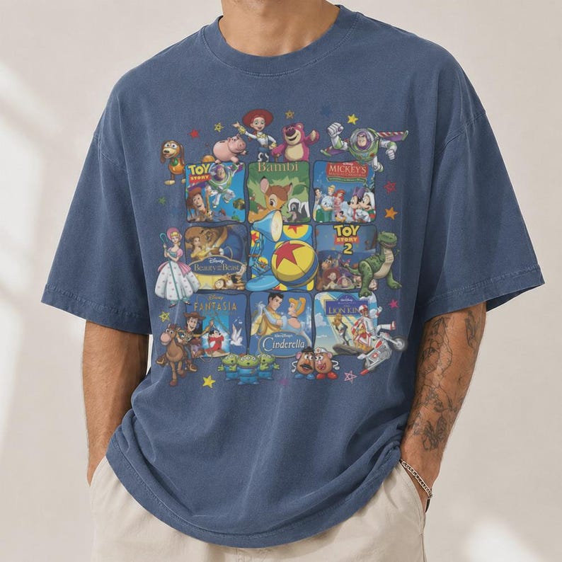 May include: Blue short-sleeved t-shirt featuring a collage of animated movie posters. The design includes images from "Toy Story," "Bambi," "Mickey's," and other classic animated films. The shirt has a relaxed fit and a crew neck.