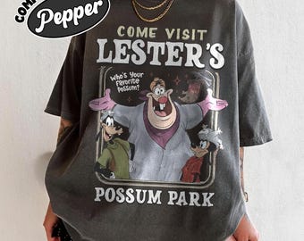 May include: Dark gray t-shirt with a graphic featuring the text "COME VISIT LESTER'S POSSUM PARK". The graphic includes cartoon characters and the phrase "Who's Your Favorite Possum?" The shirt has short sleeves and a crew neck.