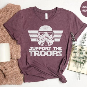 May include: A maroon heather t-shirt with a white graphic of a Star Wars Stormtrooper helmet with wings and the text "Support the Troops".