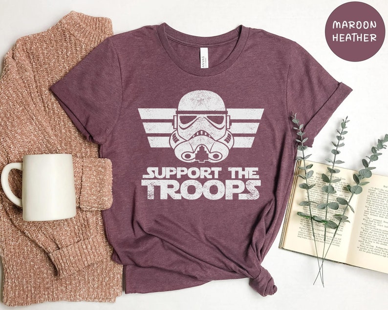 May include: A maroon heather t-shirt with a white graphic of a Star Wars Stormtrooper helmet with wings and the text "Support the Troops".