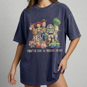 May include: Navy blue t-shirt featuring a colorful graphic of characters from the animated movie Toy Story. The text "YOU'VE GOT A FRIEND IN ME" is printed below the characters. The shirt has a relaxed fit.