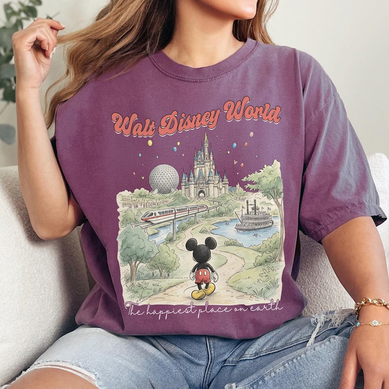 May include: A purple t-shirt featuring a vintage-style illustration of Walt Disney World. The design includes the park's castle, Spaceship Earth, a monorail, and Mickey Mouse. Text reads "Walt Disney World" and "The happiest place on earth."