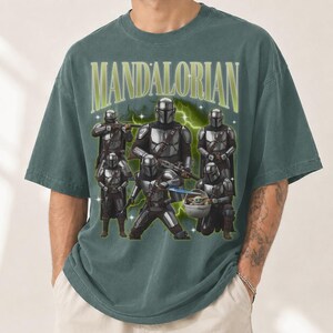 Puede incluir: Camiseta verde con la palabra "MANDALORIAN" en verde claro. El gr&aacute;fico muestra varios personajes con armadura plateada, con un beb&eacute; en un cuenco peque&ntilde;o. El fondo tiene un dise&ntilde;o de rayo.