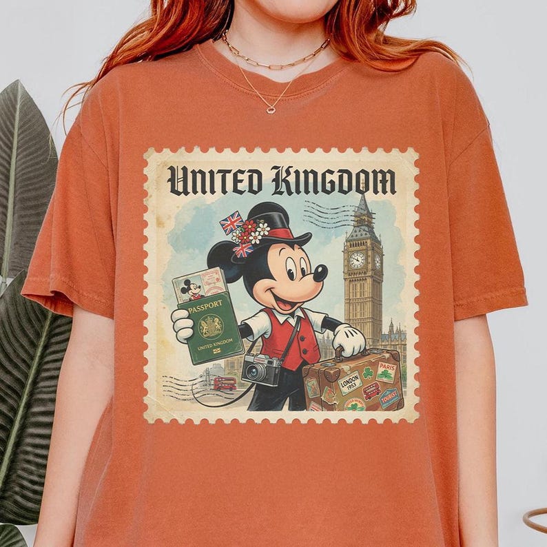Op de afbeelding: Verbrand oranje t-shirt met een vintage-stijl grafische afbeelding van Mickey Mouse als reiziger in het Verenigd Koninkrijk. Het ontwerp bevat een paspoort, koffer, camera en Big Ben. De woorden "United Kingdom" staan bovenaan.