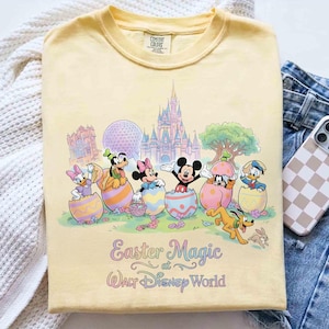 May include: Yellow Comfort Colors t-shirt featuring Disney characters emerging from Easter eggs. The graphic includes Mickey Mouse, Minnie Mouse, Donald Duck, and Goofy, with the text "Easter Magic at Walt Disney World."