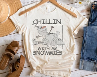 May include: A white t-shirt with a graphic of Olaf from Frozen. The graphic shows Olaf with a group of snowmen. The text on the shirt reads "Chillin' with my snowmies".