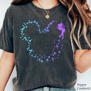 May include: A dark gray t-shirt with a blue and purple ombre design of a Mickey Mouse head made of stars. A purple fairy silhouette is blowing the stars out of a wand.