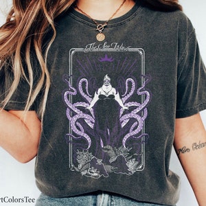 May include: A black t-shirt with a graphic of Ursula, the Sea Witch, from Disney's The Little Mermaid. The graphic is in a vintage tarot card style with purple accents. The text "The Sea Witch" is at the top of the card.