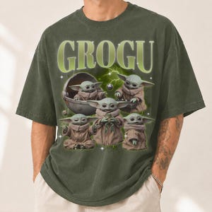 May include: Green t-shirt featuring the word "GROGU" in a light green font. The shirt displays multiple images of Grogu, a character from The Mandalorian, in various poses. The design includes a space-themed background with lightning bolts and stars.