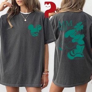 May include: Dark gray t-shirt with a green Mickey Mouse-inspired design on the front and back. The front features a stylized face, while the back displays a baseball-themed graphic with "MM 1928".