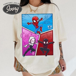 May include: Ivory-colored t-shirt featuring a comic book-style design with Spider-Man and other characters. The graphic is divided into four panels with vibrant colors and dynamic poses. The shirt has a Comfort Colors label.
