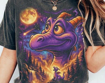 May include: A charcoal gray t-shirt featuring a large, vibrant graphic of a purple dragon with orange horns. The design includes a glowing full moon, a shooting star, a waterfall, and a smaller purple dragon in a forest setting at night.