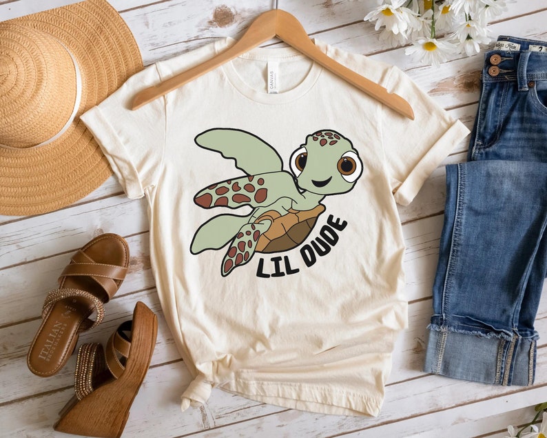 May include: A beige t-shirt with a cartoon sea turtle graphic and the text "Lil Dude".