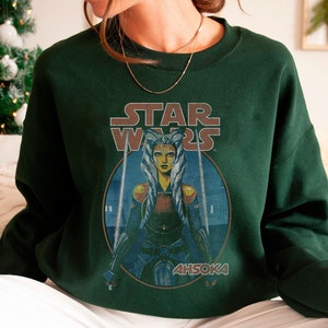 Op de afbeelding: Een donkergroen sweatshirt met een vintage Star Wars-afbeelding met Ahsoka Tano, een Togruta Jedi, met de tekst "STAR WARS" en "AHSOKA" gedrukt op de voorkant.