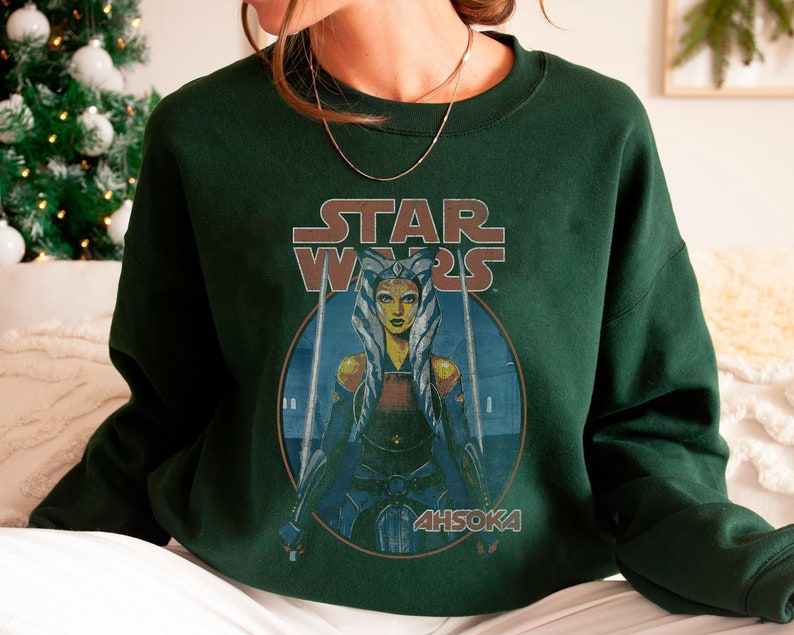 Op de afbeelding: Een donkergroen sweatshirt met een vintage Star Wars-afbeelding met Ahsoka Tano, een Togruta Jedi, met de tekst "STAR WARS" en "AHSOKA" gedrukt op de voorkant.