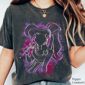 May include: A dark gray t-shirt with a purple and white outline of a woman with long hair holding a flower. The woman is wearing a dress and has a star-like pattern around her.