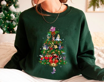 May include: A dark green sweatshirt with a Christmas tree design featuring characters from Alice in Wonderland. The tree is decorated with ornaments, lights, and a star on top. The characters include Alice, the Mad Hatter, the Cheshire Cat, and the Queen of Hearts.
