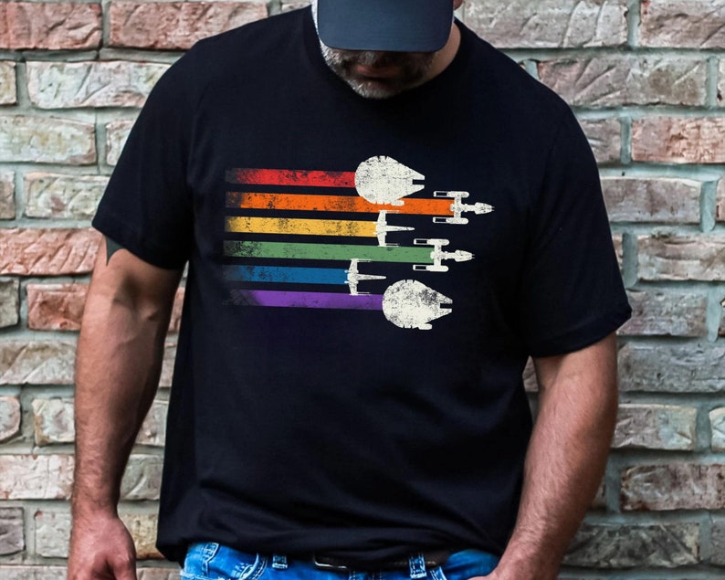 May include: A black t-shirt featuring a rainbow stripe design and a vintage-style image of Star Wars spaceships flying in formation.